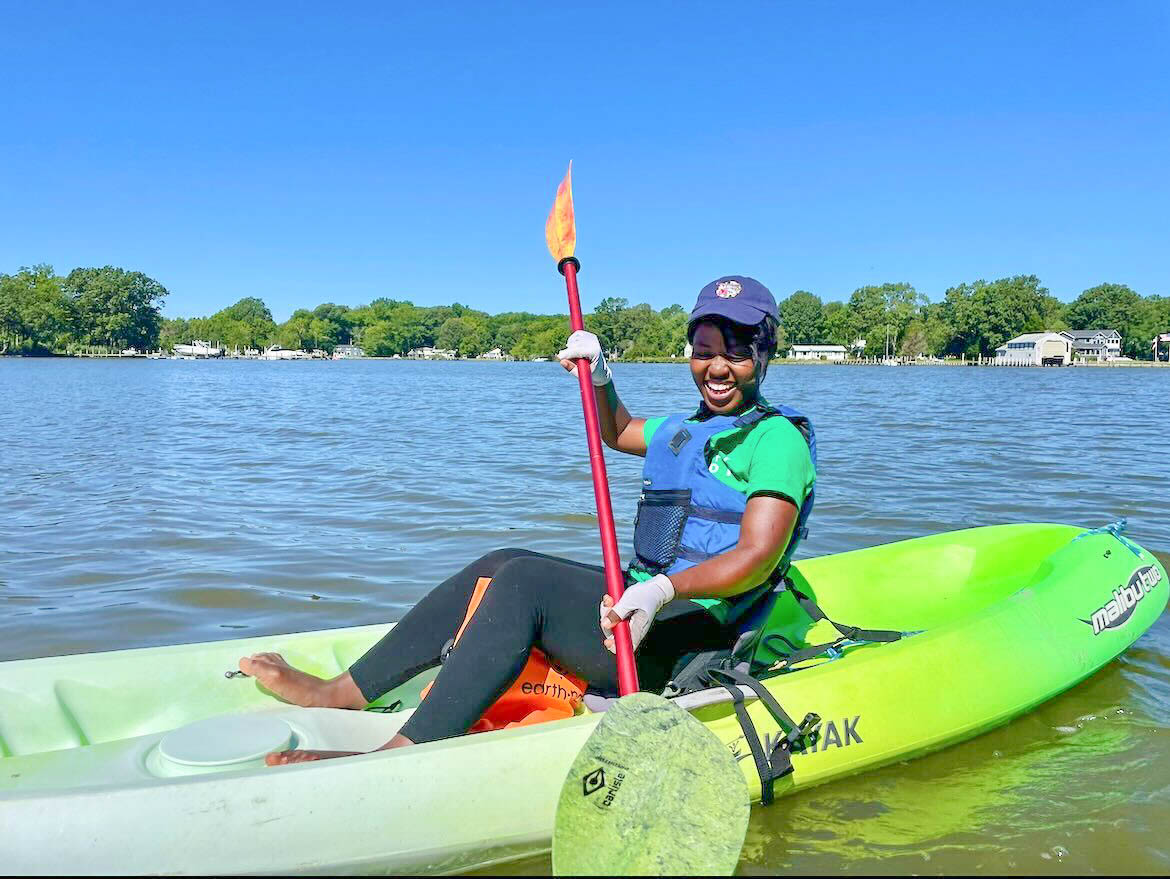 Beverly laughs while sitting in a green kayak on the Potomac river.